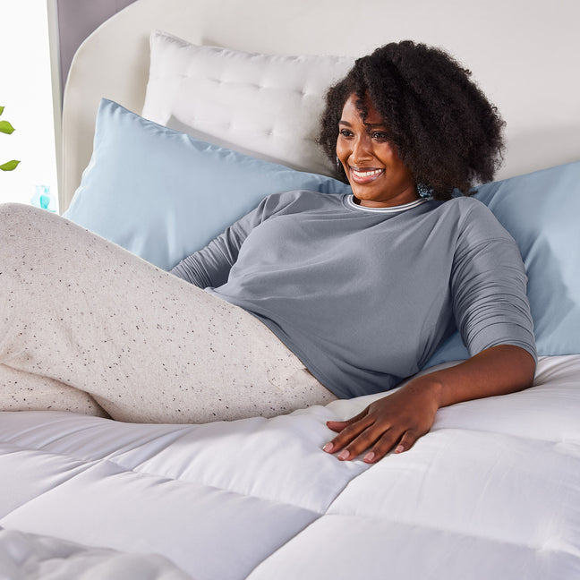 Young woman lying on the Sleep Innovations Pillow Top Mattress Pad with her hand held out to feel the quilted cover